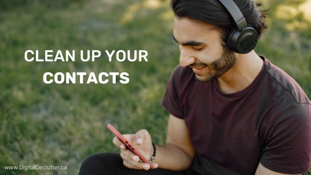 Smiling man sitting outside in the grass looking at his phone while he cleans up his contacts.