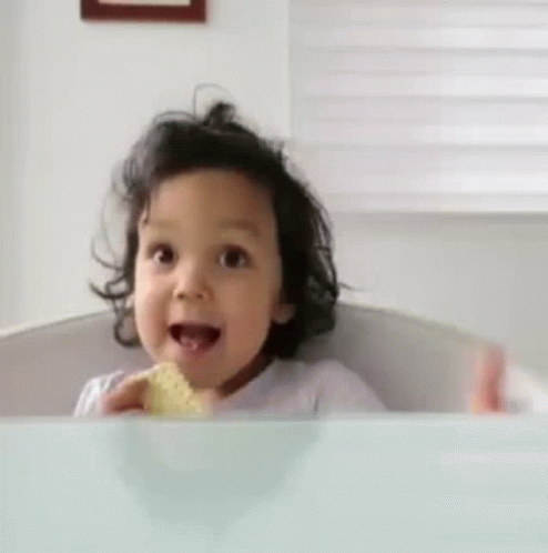 Toddler eating a sandwich giving an enthusiastic thumbs up 