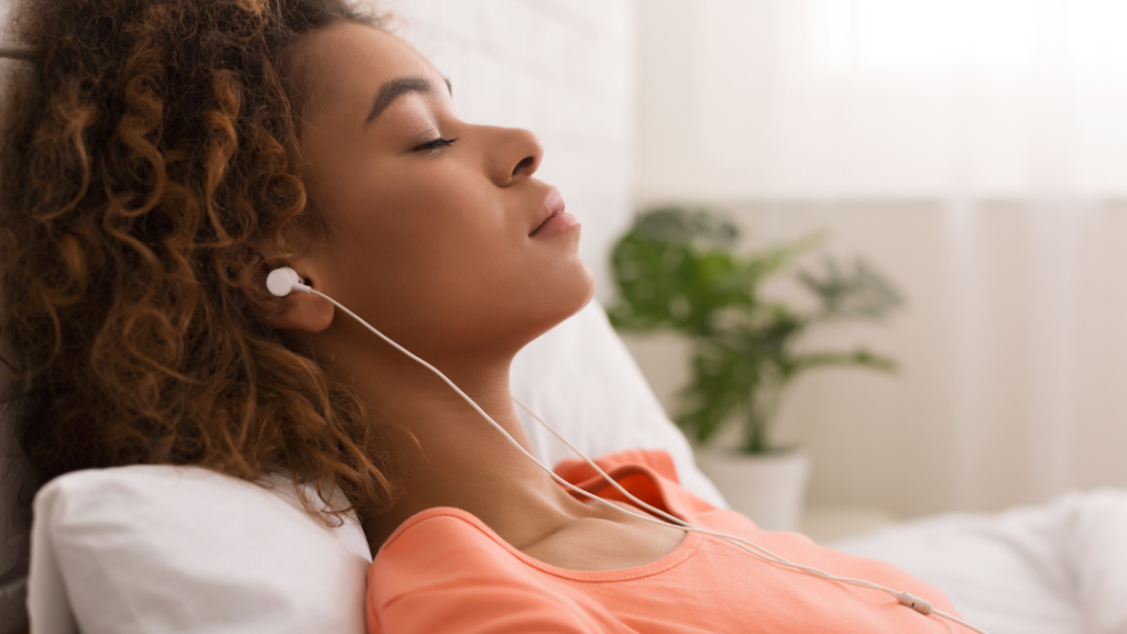 Woman laying in bed with earbuds in listening to a guided meditation to help her with her mindset on her iPhone. 