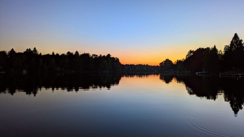 A stunning sunset over a tranquil lake, with vibrant hues of orange, yellow, and blue blending seamlessly into the horizon, symbolizing the perfect moment to unplug and embrace the beauty of nature during a vacation. This serene image encapsulates the essence of disconnecting from technology and reconnecting with oneself, encouraging viewers to immerse themselves in the richness of their surroundings.